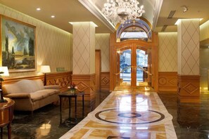 A lobby with a sofa, a coffee table, a chandelier, and a large painting on the wall. - Sina Bernini Bristol, Autograph Collection (Rome)
