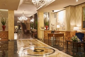 A hotel lobby with a grand chandelier, a reception desk, and a staircase in the background. - Sina Bernini Bristol, Autograph Collection (Rome)