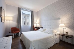 A hotel room with a large bed, two bedside tables, a desk, a chair, and a window with curtains. - Sina Bernini Bristol, Autograph Collection (Rome)