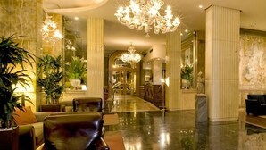 A lobby with a marble floor, leather chairs, a reception desk, and a chandelier. - Sina Bernini Bristol, Autograph Collection (Rome)