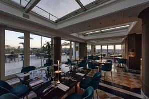 A rooftop dining area with tables and chairs, large windows, and a view of the cityscape. - Sina Bernini Bristol, Autograph Collection (Rome)