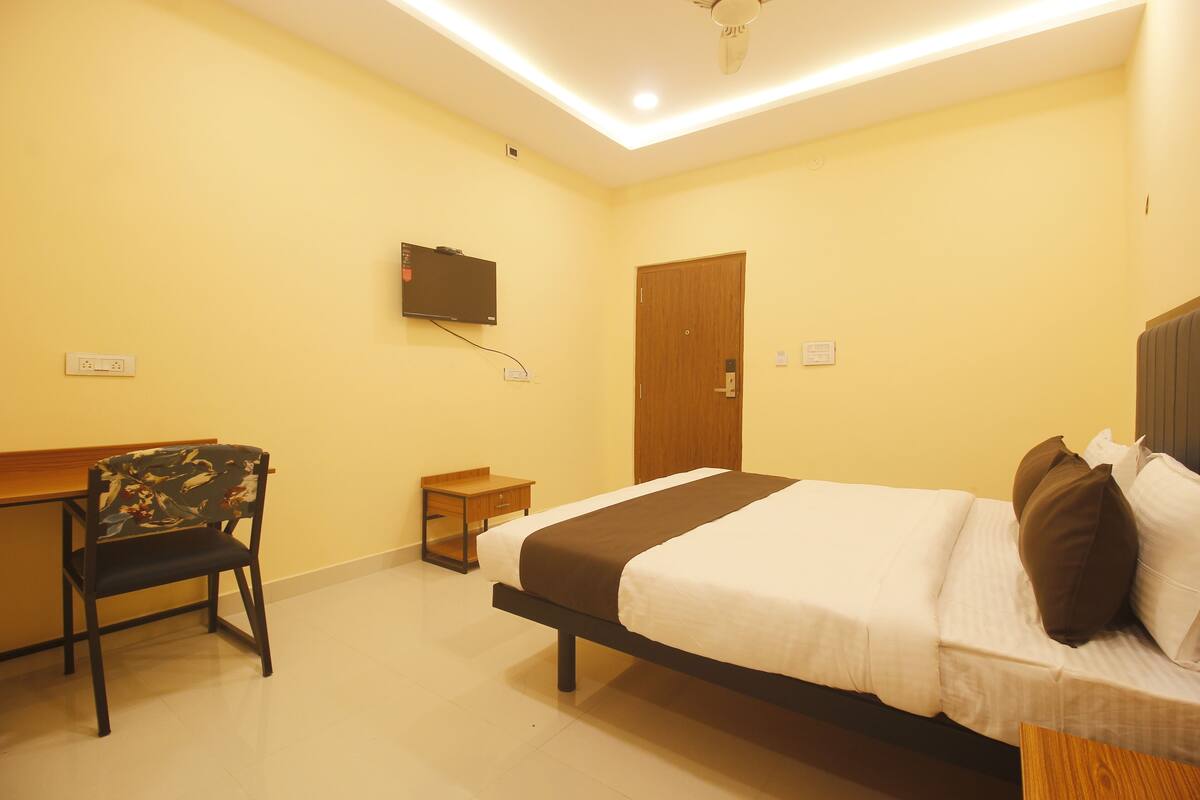 A hotel room with a bed, a desk, a chair, and a television on the wall.
