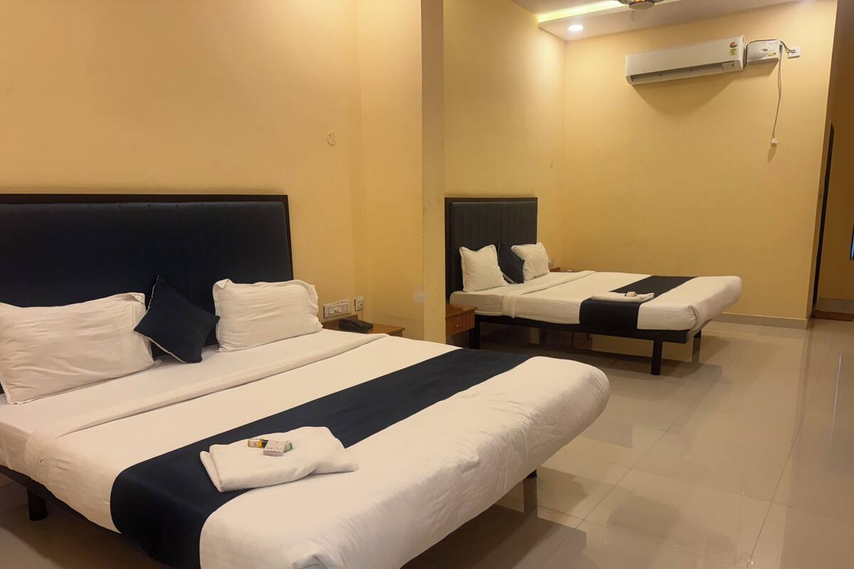 A hotel room with two beds, each with white linens and dark headboards. There is a bedside table with a phone and a lamp on each bed.