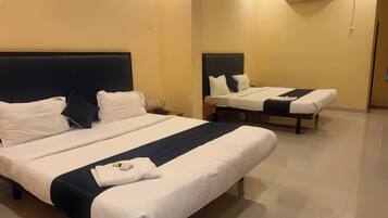 Habitación de hotel con dos camas, cada una con ropa blanca y cabeceros oscuros. En cada cama hay una mesita de noche con un teléfono y una lámpara.