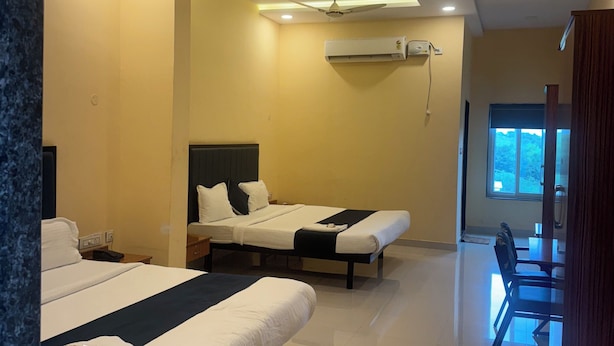 A hotel room with two beds, a ceiling fan, an air conditioning unit, and a dining area with a table and chairs. - HOTEL MINT PARK (Balanagar)