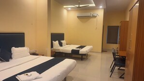 A hotel room with two beds, a desk, a chair, an air conditioning unit, and a ceiling fan. - HOTEL MINT PARK (Balanagar)