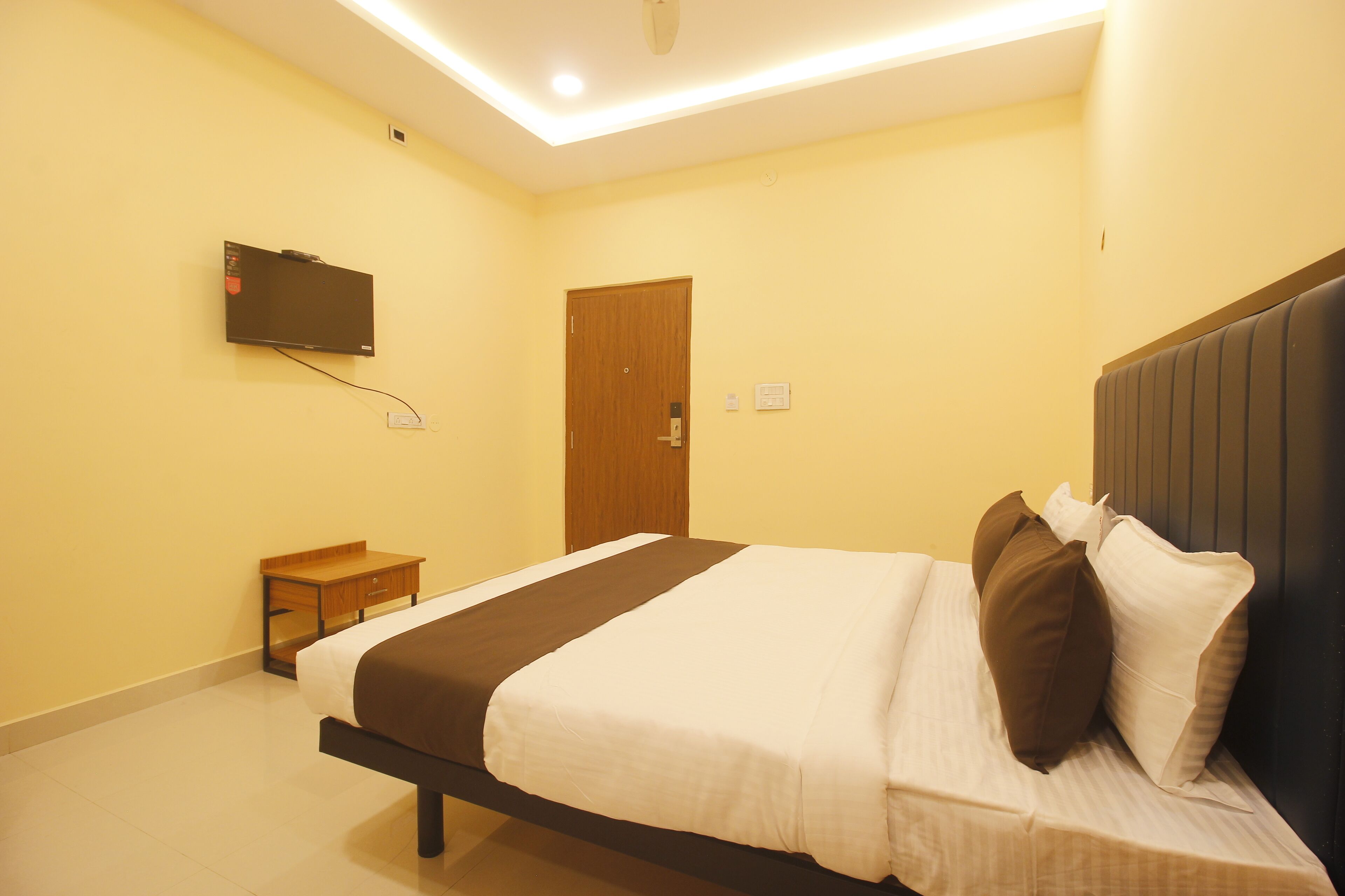 A hotel room with a bed, a television mounted on the wall, a bedside table, and a door.