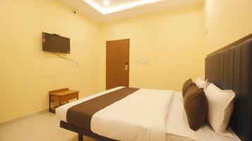 A hotel room with a bed, a television mounted on the wall, a bedside table, and a door.