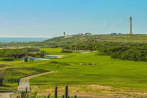 A golf course with bunkers, a water hazard, a lighthouse, and a building on a hill. - LUX 3BR House Pool Gym 7-Min Walk Palm Beach - Porta Al Sole 6 by Bocobay (Noord)