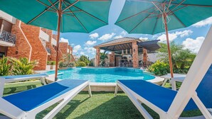 A swimming pool with lounge chairs and umbrellas, surrounded by brick buildings and greenery. - LUX 3BR House Pool Gym 7-Min Walk Palm Beach - Porta Al Sole 6 by Bocobay (Noord)
