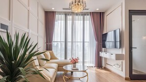 A modern living room with a beige sofa, a glass coffee table, a potted plant, and a TV mounted on the wall. - Vinhomes Skylake Lynn Housing (Hanoi)