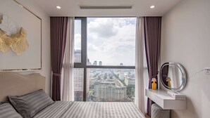 A bedroom with a large window, a bed, a vanity with a mirror, and a city view. - Vinhomes Skylake Lynn Housing (Hanoi)
