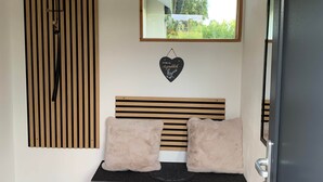 Une pièce avec un mur recouvert de lambris en bois, un miroir, une décoration en forme de cœur, un banc avec des coussins et une porte.