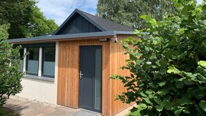 Un petit bâtiment en bois, doté d’une porte sombre et d’une fenêtre, entouré de verdure.