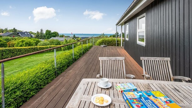 Eine Holzterrasse mit Tisch, Stühlen und Blick auf das Meer.