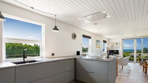 Eine moderne Küche mit einer großen Kochinsel, einem Essbereich mit Stühlen und Blick auf das Meer.