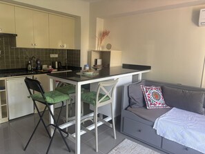 Une cuisine compacte comprenant un coin repas, un petit réfrigérateur et un canapé agrémenté d’un coussin décoratif.