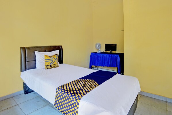 A neatly made bed with a white and blue patterned bedspread, a blue table with a fan, and a black monitor on the side. - SPOT ON 92480 Iwn Homestay Syariah (Banyuwangi)