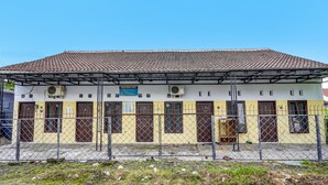 A building with a tiled roof, multiple doors, and a fenced area. - SPOT ON 92480 Iwn Homestay Syariah (Banyuwangi)