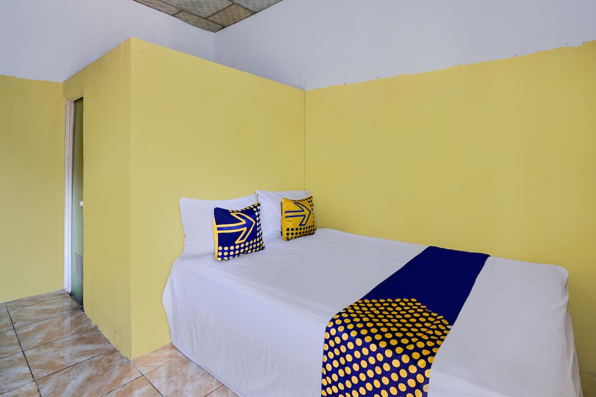 Una habitación con paredes amarillas, una cama con ropa de cama blanca y almohadas azules y amarillas, y un piso de baldosas.