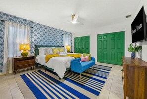 Um quarto com uma cama, um sofá azul, um guarda-roupa verde, uma mesa de cabeceira de madeira e uma televisão.