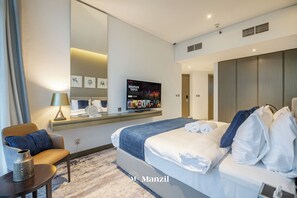 A modern hotel room with a large bed, a desk with a lamp, a flat-screen TV, and a mirror.