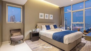 Ett modernt hotellrum med en stor säng, ett nattduksbord, en stol och utsikt över stadsbilden genom stora fönster.