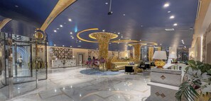 Eine großzügige Lobby mit Marmorboden, einer Rezeption, einer Sitzecke mit Sofas und einer großen, dekorativen Säule.