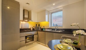 Eine moderne Küche mit Edelstahlgeräten, ein Essbereich mit Tisch für Zwei und ein Fenster mit Blick auf die Stadt.