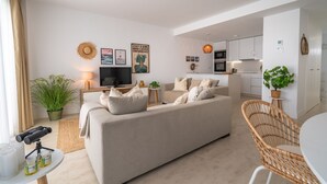 A modern living room with a sofa, a television, and a dining area with a wicker chair. - Experience Elevated Living at this Pure South Penthouse (Manilva)