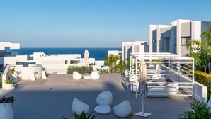A modern rooftop terrace with white architectural features, seating areas, and a view of the sea. - Experience Elevated Living at this Pure South Penthouse (Manilva)