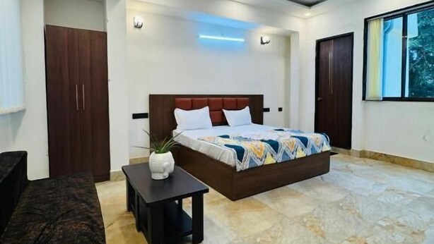 Un dormitorio con cama, ventilador de techo, mesita de noche, planta en maceta y ventana.