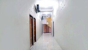 A narrow, well-lit hallway with tiled flooring, wooden doors, and a staircase at the end. - SPOT ON 2629 Duta Karimun (Karimun Jawa)