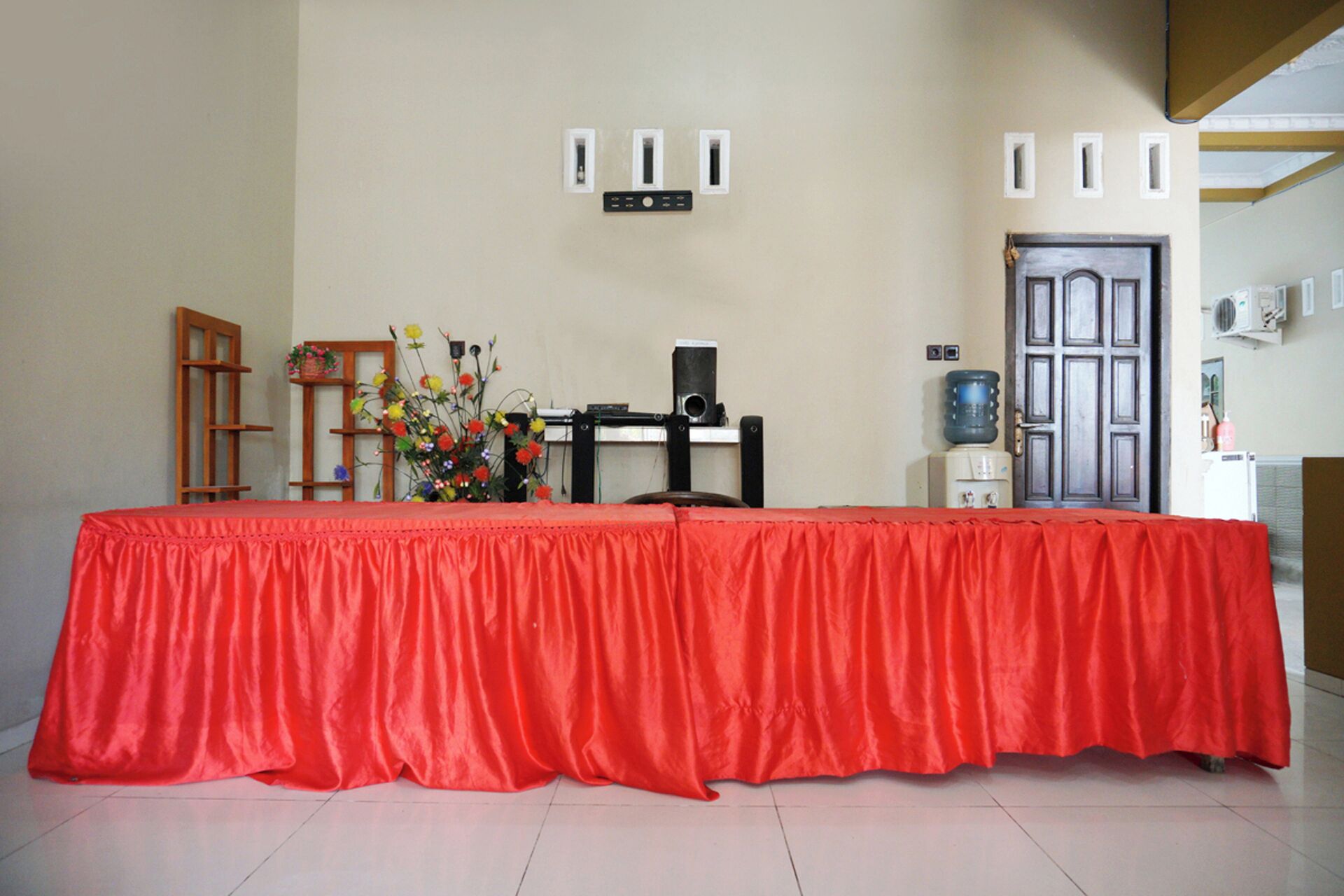 A room with a red table, a wooden chair, a water dispenser, and a door.