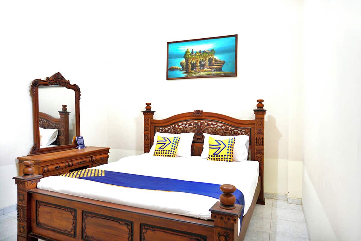 A wooden four-poster bed with a blue and yellow bedspread, two pillows with arrow designs, and a wooden nightstand with a mirror.