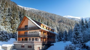 A two-story wooden building with balconies, surrounded by snow-covered trees and mountains. - Hotel Esprit (Špindlerův Mlýn)