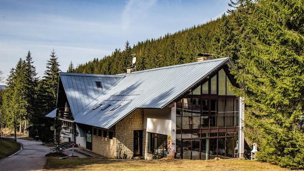 A modern building with a sloped roof, large windows, and a stone facade, surrounded by a forested area. - Hotel Esprit (Špindlerův Mlýn)