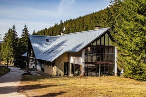 A modern building with a sloped roof, large windows, and a stone facade, surrounded by a forested area. - Hotel Esprit (Špindlerův Mlýn)