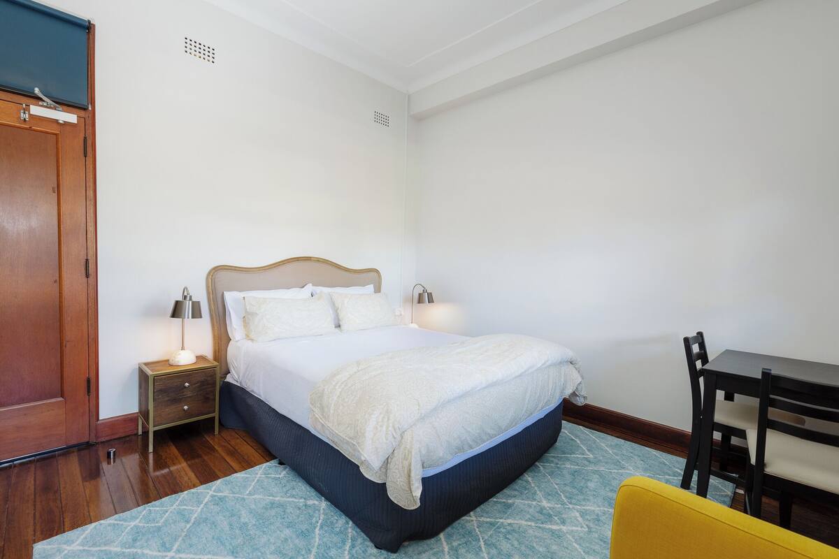 A neatly made bed with a wooden headboard, a bedside table with a lamp, and a small chair.