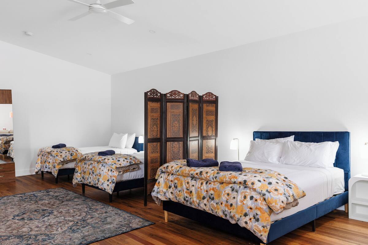 A bedroom with a large bed, two smaller beds, a wooden partition, and a patterned rug.