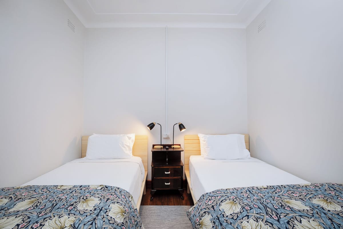 A twin room with two beds, a nightstand with lamps, and a wooden floor.