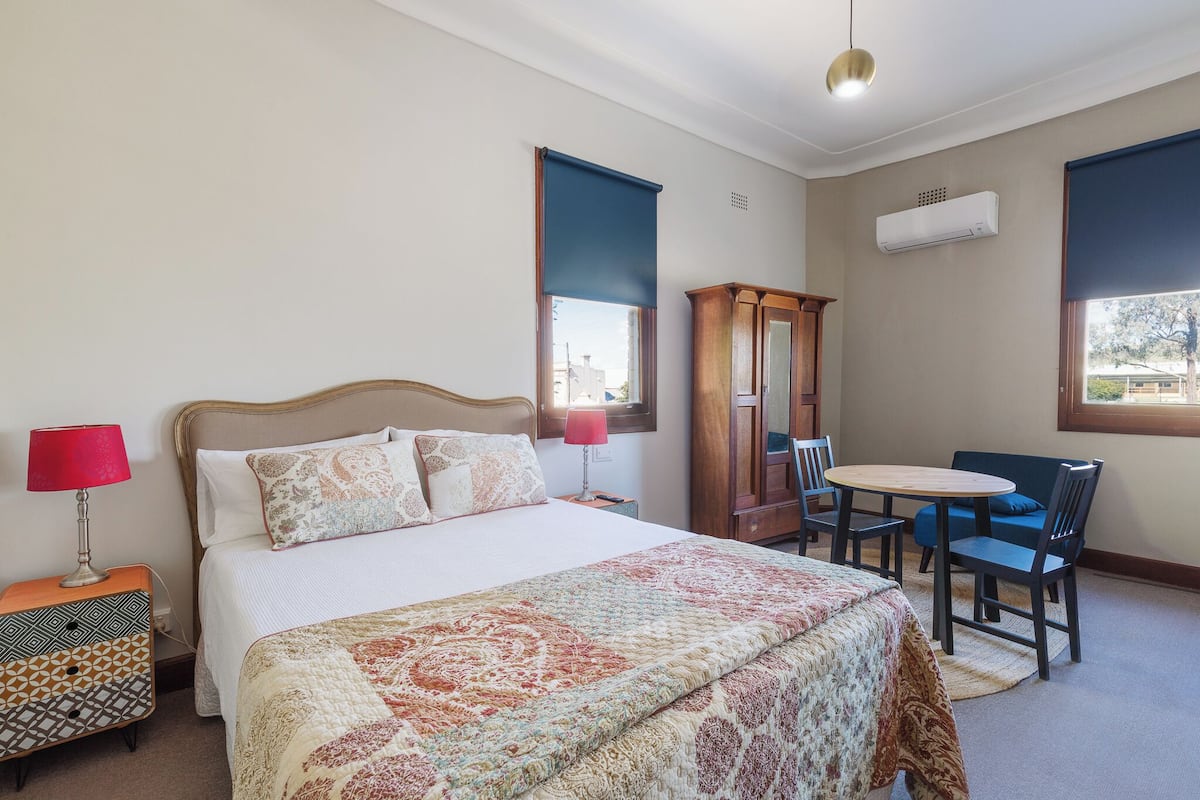 A bedroom with a bed, bedside table, lamp, dresser, chair, and a small table with a chair.