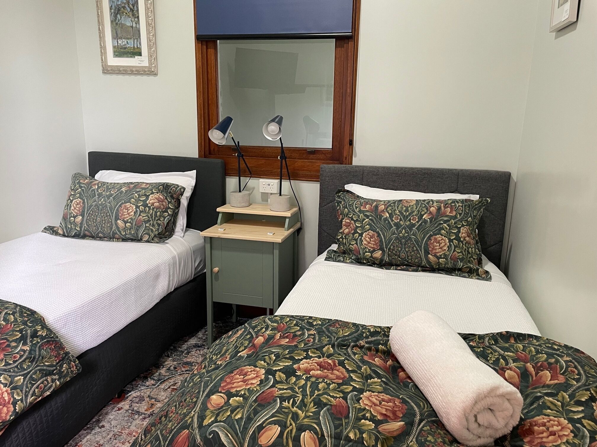 Habitación doble con dos camas, cada una con ropa de cama de motivos florales, una mesita de noche pequeña y un espejo sobre la cama.