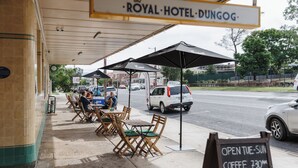 An outdoor seating area of the Royal Hotel Dungog with tables and chairs, umbrellas, and a sign indicating opening times for coffee and the bar. - Royal Hotel Dungog (Dungog)
