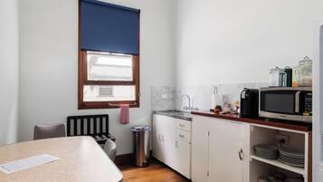 Una cocina compacta con área de comedor, una ventana con persiana azul, un bote de basura de acero inoxidable y un microondas en la encimera.