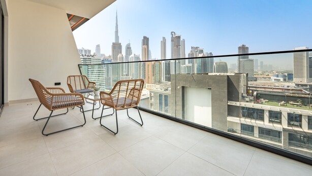 A balcony with wicker chairs and a table, overlooking a cityscape with modern buildings. - Canal and Burj Khalifa Views, Mins Drive to Downtown Dubai (Dubai)
