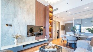 A modern living room with a flat-screen TV, a dining area with a round table, and a kitchen visible through an open door. - Canal and Burj Khalifa Views, Mins Drive to Downtown Dubai (Dubai)