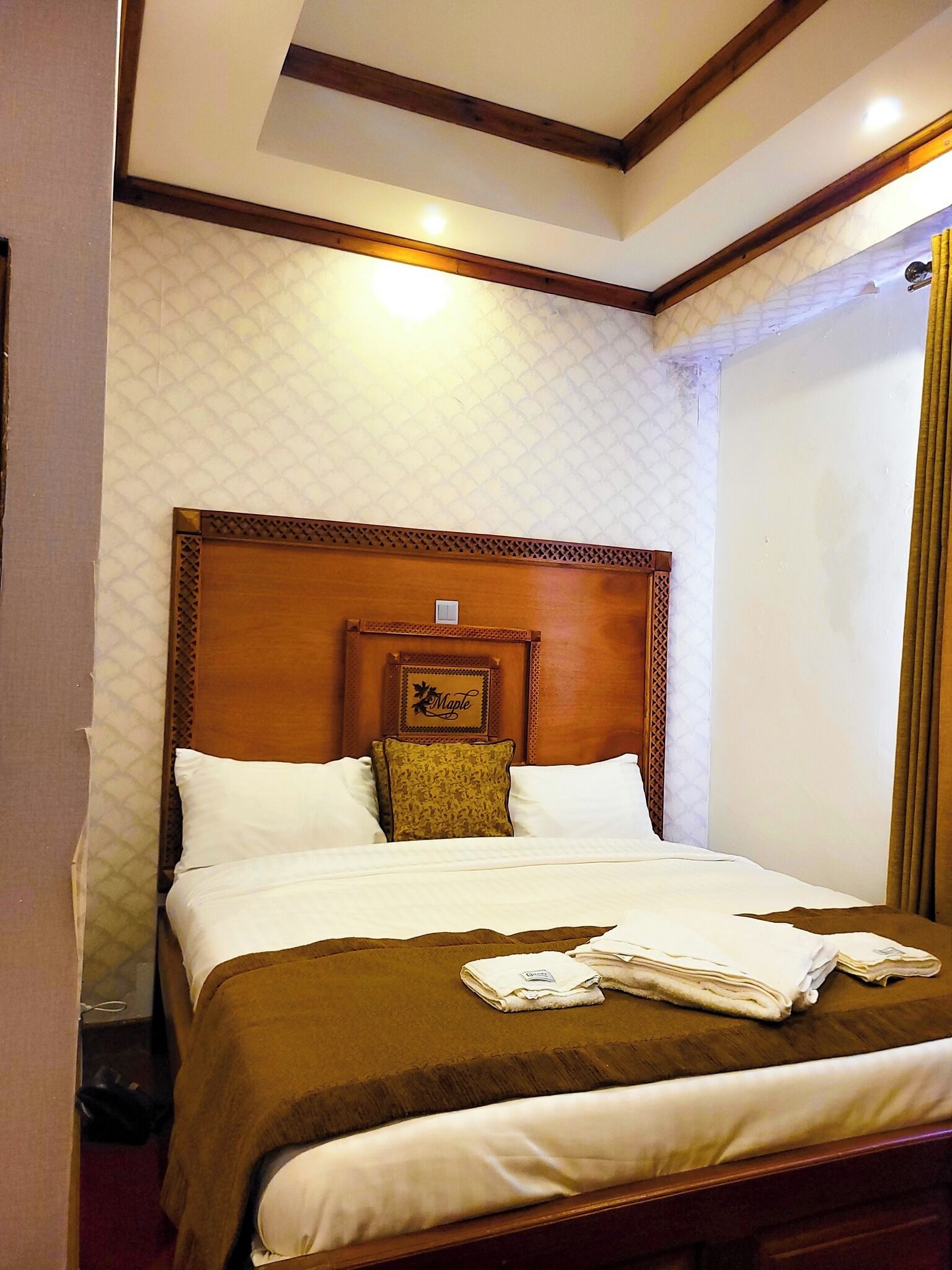 A hotel room with a large bed, wooden headboard, and a quilted wall pattern.