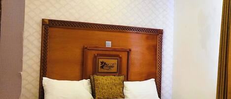 A hotel room with a large bed, wooden headboard, and a quilted wall pattern.