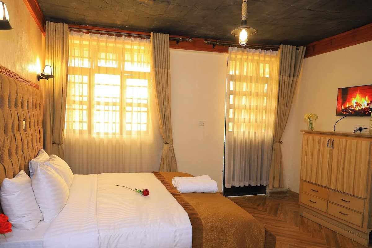 A bedroom with a large bed, a wooden headboard, a wooden dresser, and a fireplace on the wall.
